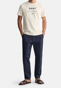 Krémové bavlněné tričko s námořnickým potiskem, kombinované s námořnickými chinos kalhotami a hnědými koženými sandály. Minimalistický design, uvolněný střih.