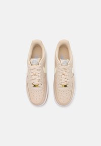 Light beige sneakers with perforated toe, cream accents, golden hardware on the lace, and white sole. Smooth leather texture.