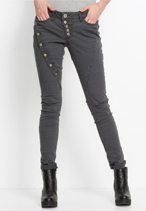 Jean skinny gris avec un devant à boutons, des poches diagonales uniques et un ourlet roulé. Accompagné de bottines noires.