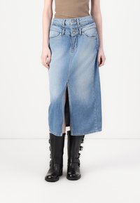 Fustă din denim de culoare albastru deschis, cu o deschidere frontală, închidere cu două nasturi și bucle pentru curea. Asortată cu cizme negre până la genunchi.