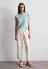 Helles blaues Kurzarm-T-Shirt, cremefarbene Leinenhose mit Kordelzug und tanfarbene, gewebte Sandalen. Einfacher, lockerer Schnitt, weiche Texturen und helle Farben.