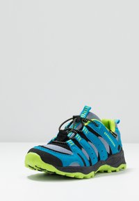 Zapato de senderismo azul y gris con acentos en negro y verde, que presenta una suela texturizada, cordones elásticos y una puntera reforzada. Diseño ligero.