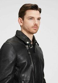 Schwarze Leder-Motorradjacke mit durchgehendem Reißverschluss, Druckknopfkragen und Schnallen-Detail. Verfügt über eine glatte Textur und eine taillierte Silhouette.