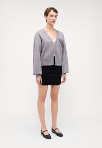 Vaaleanharmaa lyhyeksi leikattu neuletakki, jossa on ylisuuria hihoja, neulotettu pinta ja nappiyksityiskohta. Yhdistetty mustaan, istuvaan hameeseen ja mustiin ballerinoihin.