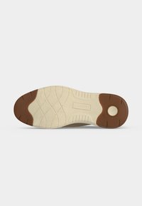 Semelle de chaussure avec surface texturée beige et zones en caoutchouc marron au talon et à la pointe, avec un insert circulaire au talon et le nom de la marque embossé au centre.
