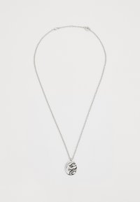 Srebrna verižica z ovalnim obeskom, ki ima črn vzorec z zmajem in zapletenim okrasjem. Veriga ima teksturiran zaključek.