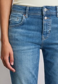 Blauwe denim jeans met een licht vervaagde afwerking, voorzien van twee knopen bij de taille, subtiele stiksels en een voorzak.