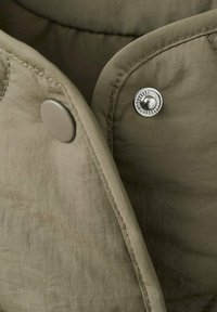 Nærbillede af khakifarvet stof med to trykknapper, en mat beige og en blank sølv, der viser syningsdetaljer.