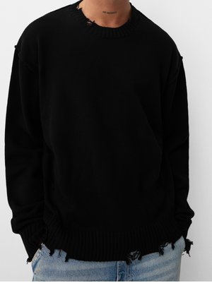 Černý oversized pletený svetr s distressed detaily na výstřihu a spodním lemu. Žebrované manžety a spodní okraj. Nosené s světle modrými džíny.
