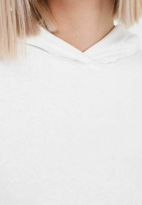 Vit hoodie tillverkad av mjukt tyg, med dragsko i huvan och en slät, texturerad yta. Inga mönster eller metallbeslag synliga.