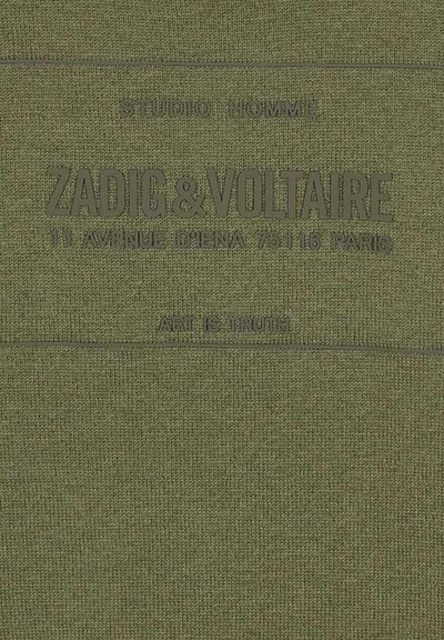 Groene textiel met reliëftekst. Merkennaam "ZADIG&VOLTAIRE" en adres gedrukt boven de zin "KUNST IS WAARHEID" onderaan.