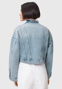 Chaqueta de denim recortada en azul claro con cuello deshilachado, costuras prominentes y mangas largas con puños abotonados.
