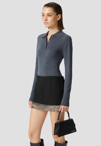 Polo a maniche lunghe di colore blu navy con colletto e bottoni, abbinato a una mini gonna nera con orlo decorativo e scintillante, mentre tiene una borsa nera.