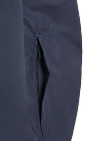 Gros plan d'une manche de veste bleu marine montrant une poche à fermeture éclair verticale partiellement ouverte.