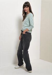 Jasnozielona, w paski, bluzka z długim rękawem zestawiona z ciemnoszarymi spodniami prostymi, w klasycznym kroju, oraz białymi trampkami.