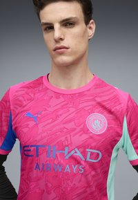 Rosa Manchester City-tröja med blå och mintgröna accenter, med ett texturerat mönster, Puma-logotyp och Etihad Airways-märke.