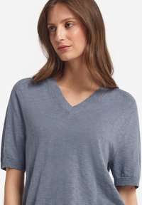 Ljusblå, kortärmad stickad tröja med V-halsdesign. Har en mjuk textur och subtila ribbade detaljer vid halsringning och ärmslut.