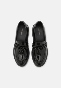 Mocassins en cuir verni noir avec un accent de chaîne tissée sur le devant, semelle plate et design à bout arrondi.