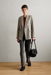 Blazer rayé gris sur un top rouille, associé à un jean droit gris et des chaussures à plateforme noires, tenant un sac à main noir avec une bandoulière.