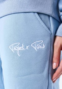 Lichtblauwe joggers van zachte stof, met een witte geborduurde logo "Project x Paris" op het voorzakgebied en een geribbelde tailleband.