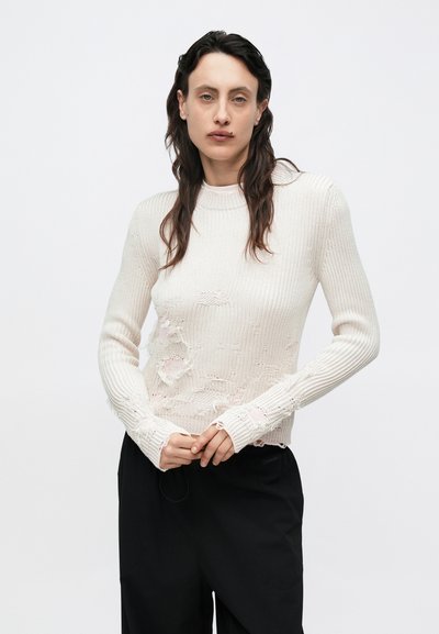 Pulover alb tricotat cu dungi, cu detalii deteriorate  și margini destrămate, mâneci lungi, gât rotund, asortat cu pantaloni negri largi.