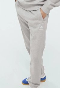 Svetlosivé teplákové nohavice vyrobené z bavlnenej zmesi, s vreckami a bielym logom Adidas na hornej časti stehna, so zužujúcim strihom.