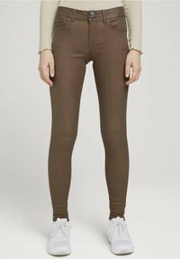 Vaqueros ajustados marrones en una mezcla de algodón suave, con cierre de botón, trabillas para el cinturón, bolsillos delanteros y un diseño ceñido, combinados con zapatillas blancas.