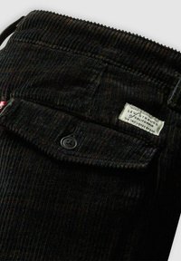 Pantaloni di velluto a coste neri con righe verticali, chiusura con bottone e un'etichetta cucita con il marchio Levi Strauss sulla vita.