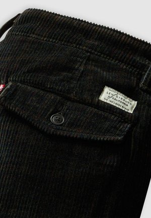Pantalones de pana negra con canalones verticales, cierre de botón y una etiqueta cosida con la marca Levi Strauss en la cintura.