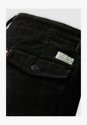 Zwarte corduroy broek met verticale ribbels, een knoopsluiting en een genaaid etiket met Levi Strauss branding op de tailleband.