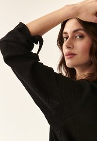 Black textured top with long puffed sleeves, featuring a button detail at the cuff. Fabric appears lightweight and slightly crinkled.