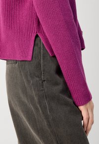Fuchsia knitted sweater with ribbed texture and side slits, paired with dark gray high-waisted trousers. Close-up of sleeve and waist.