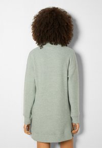 Robe en maille vert clair à manches longues avec un col montant et une coupe décontractée, présentant des fentes latérales et une longueur mi-cuisse.