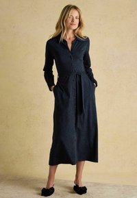 Dlhé rukávy, tmavomodré šaty so vzorom leopardí, zapínanie na gombíky vpredu, opasok v páse a bočné vrecká. Nosené s čiernymi papučami s mašľou.