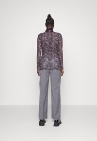 Durchsichtige Langarmbluse mit floralem Muster in Dunkelgrau, kombiniert mit grauen, lockeren, plissierten Hosen und schwarzen Schuhen, von hinten betrachtet.