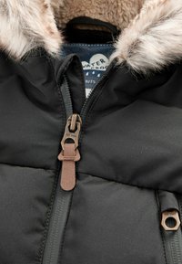 Schwarze Winterjacke mit fellgefütterter Kapuze, teilweise zugezippt an der Vorderseite und sichtbarem wasserdichtem Etikett im Kragen.