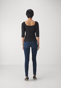 Top negro texturizado de manga larga con un corte cuadrado en la espalda, combinado con unos jeans skinny azul oscuro y tacones negros con acentos en verde neón.