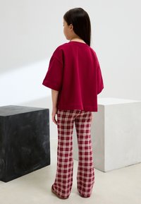 Bordeauxrotes oversized T-Shirt mit kurzen Ärmeln, kombiniert mit karottenförmigen Hose in Rot- und Cremetönen. Glatte Baumwollstruktur, lockere Passform.