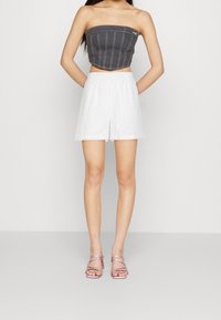 Haut court sans manches gris avec un short taille haute texturé blanc, présentant un motif subtil, associé à des talons roses à lanières.