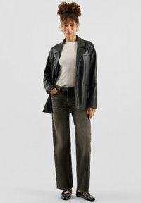 Schwarzer Lederblazer über einem hellen Pullover mit kleinen Verzierungen, kombiniert mit hoch taillierten, dunkelgrünen Jeans mit weitem Bein und schwarzen Slip-on-Schuhen.