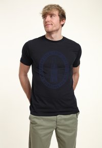 Czarny t-shirt wykonany z gładkiej bawełny, z okrągłym nadrukiem logo przedstawiającym klasyczną butelkę Coca-Coli oraz tekstem w ciemnoniebieskim kolorze.