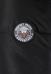 Tela negra con un parche bordado circular. El parche incluye "RESPECT BRAND" y "ADVENTURE" con montañas y estrellas, fechado en 1997.