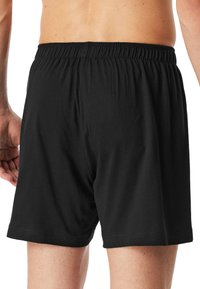 Shorts en coton noir avec une taille élastique, dotés d'une coupe décontractée et d'une texture douce, se terminant juste au-dessus des mi-cuisse.