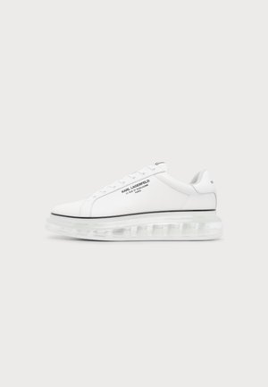 Biały niski sneaker z przezroczystą grubą podeszwą i czarnym napisem "Karl Lagerfeld" z boku na jednolitym tle.