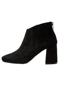 Bottine en daim noir avec bout pointu, talon carré et fermeture éclair latérale, présentant une texture lisse et une silhouette élégante.