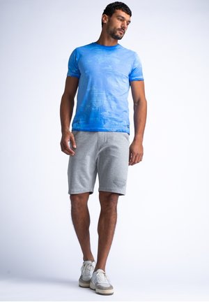 Blue short-sleeve T-shirt with a subtle textured pattern, paired with light gray shorts and beige sneakers.