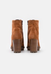 Stivaletti in suede marrone con cerniera laterale, punta rotonda e tacco spesso e texturizzato. Dettagli in pelle liscia vicino alla suola.