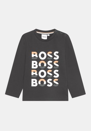 Schwarzes Langarmshirt für Kleinkinder mit vier übereinander gestapelten "BOSS"-Logos in Weiß, Grau und Pfirsich sowie drei Druckknöpfen an der Schulter.