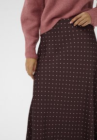 Falda marrón con lunares rosas, diseño fluido, tela suave. Suéter rosa de punto con textura acanalada, ajuste ligeramente oversize.