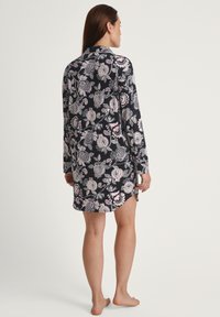 Abito a maniche lunghe in tessuto blu navy con motivi floreali bianchi e rosa, caratterizzato da un colletto a camicia e spacchi laterali all'orlo, vista posteriore.